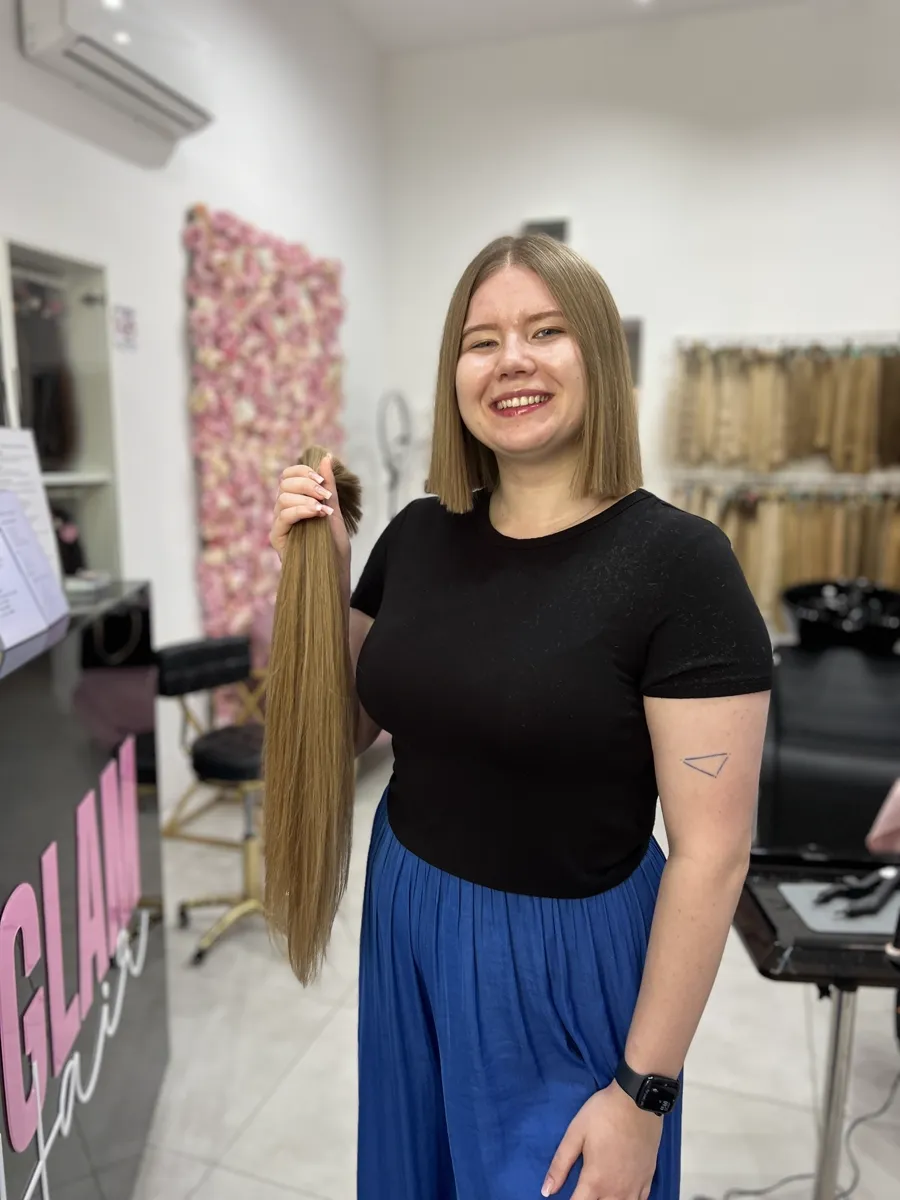Klientka po ścięciu, trzymająca własną kitkę w salonie